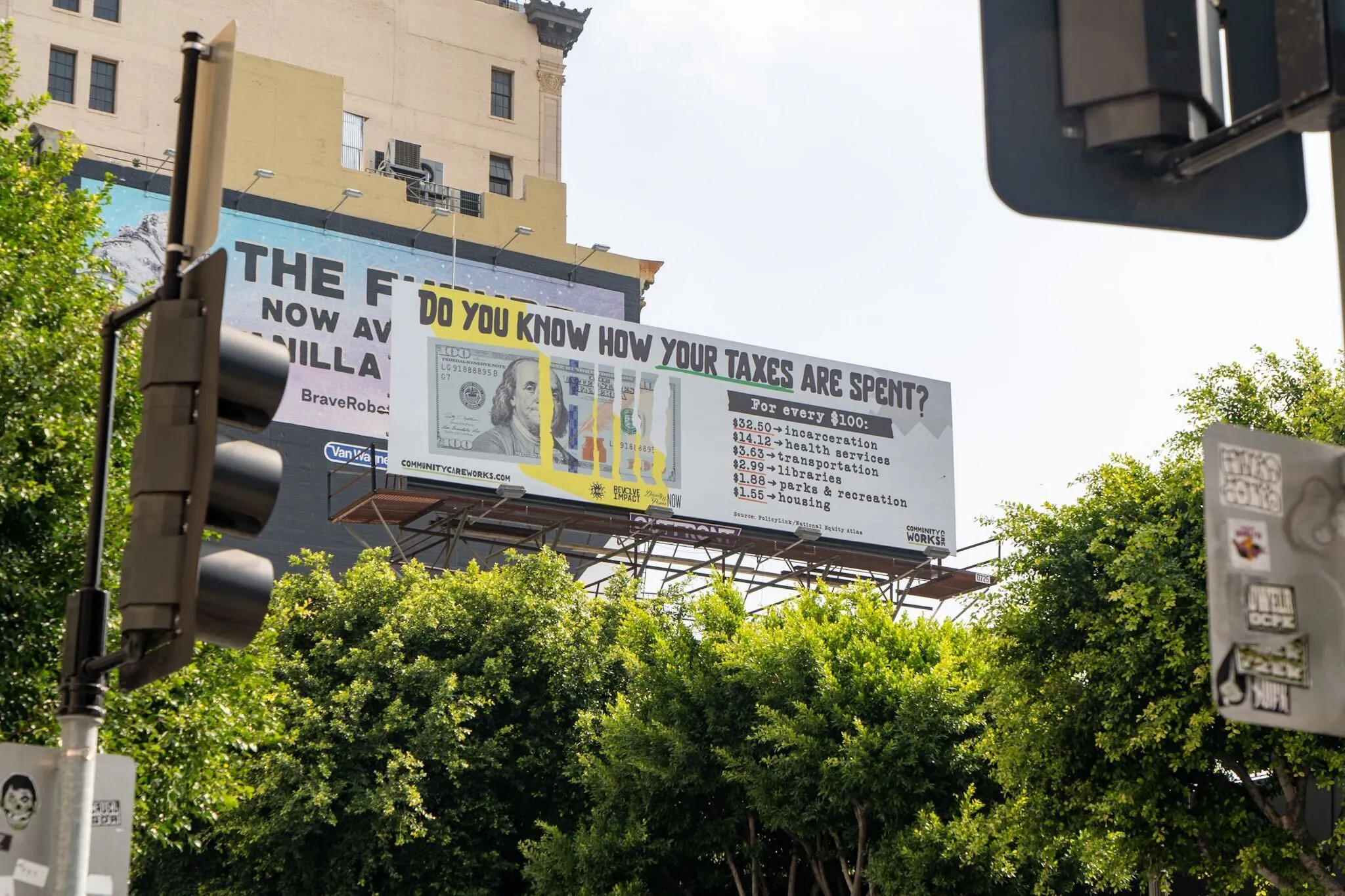 Static billboard above a Los Angeles street. The cut hundred dollar bill carrying the budget breakdown.