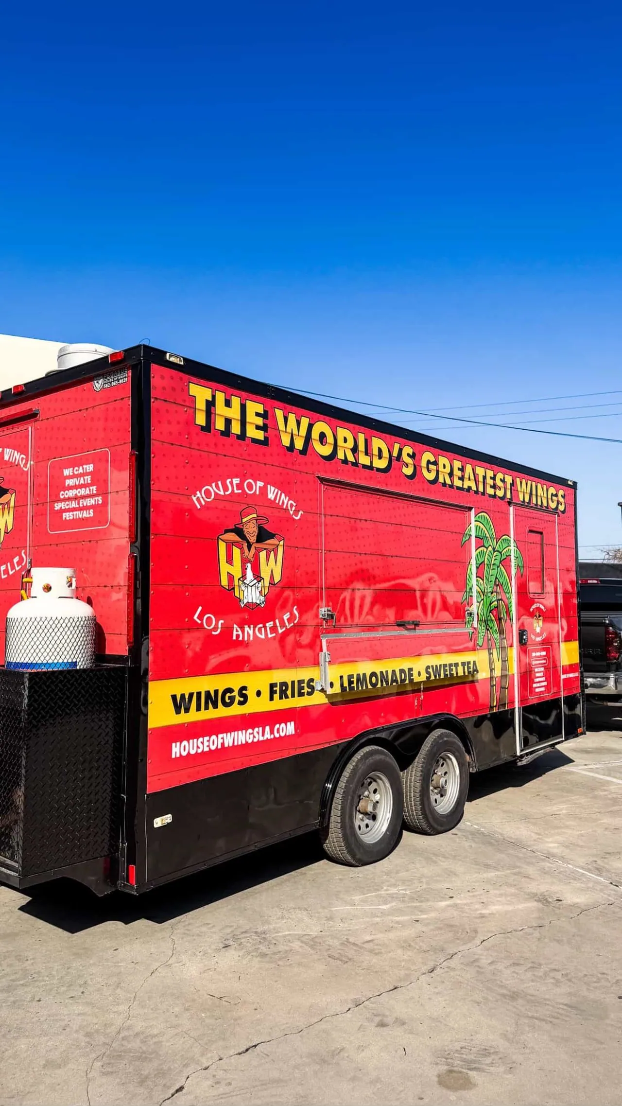 The finished trailer on a Los Angeles lot, three quarter view. High contrast red and yellow wrap with the House of Wings mark, built to be read from down the block.