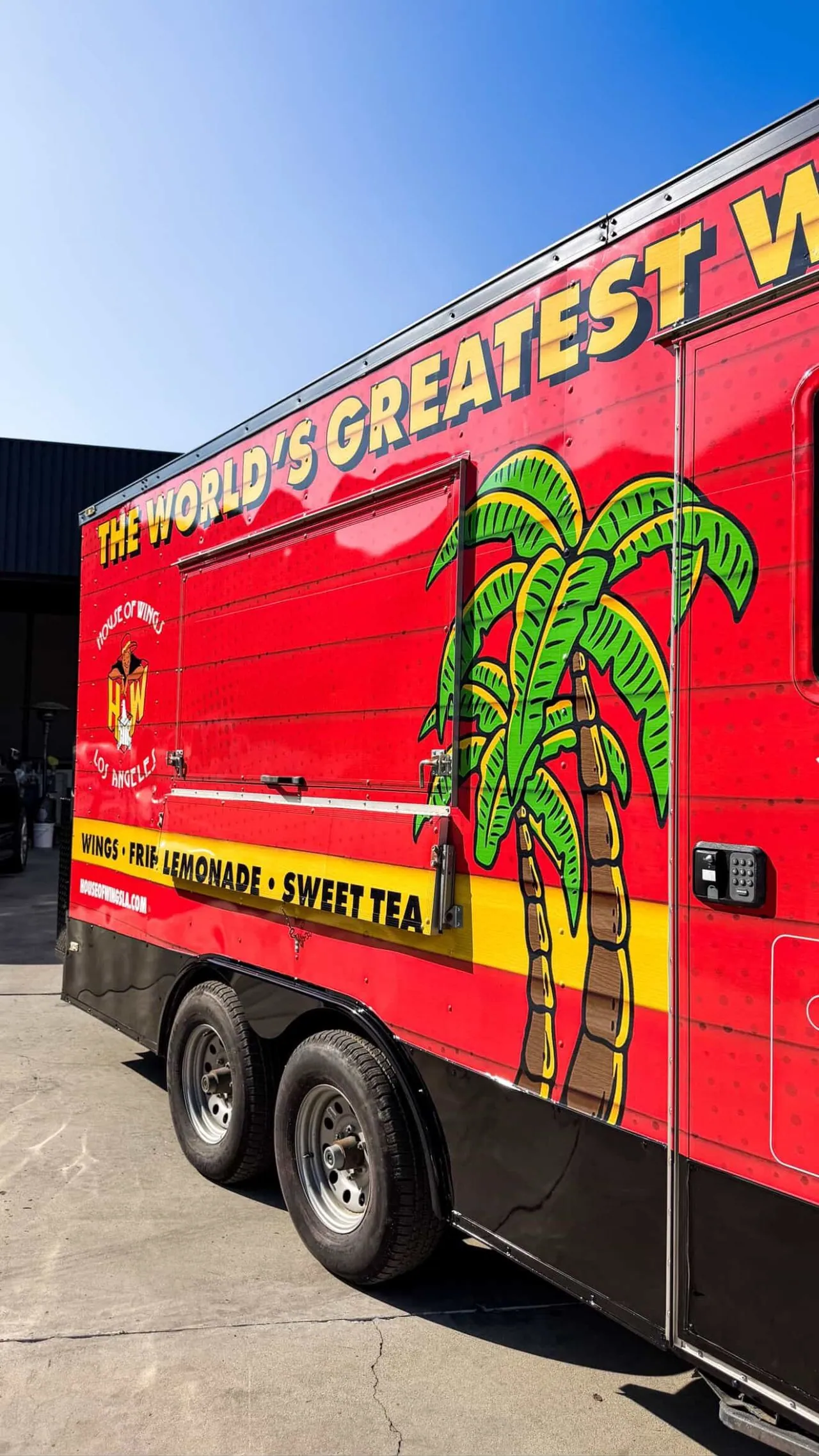 Service side of the trailer with the window open. Palm illustration, the menu strip in yellow, and the mark at eye level for anyone in line.