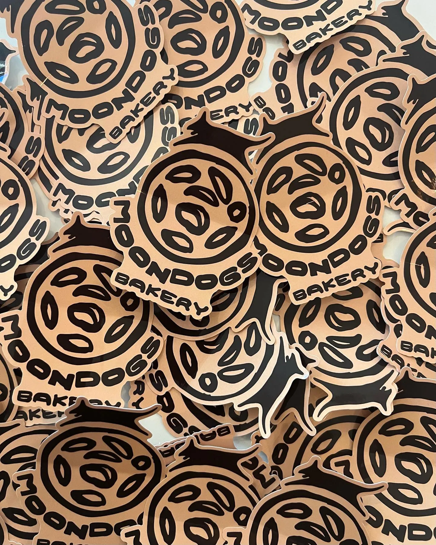 Die cut stickers piled by the hundred, the mark reversed in brown on a warm tan.